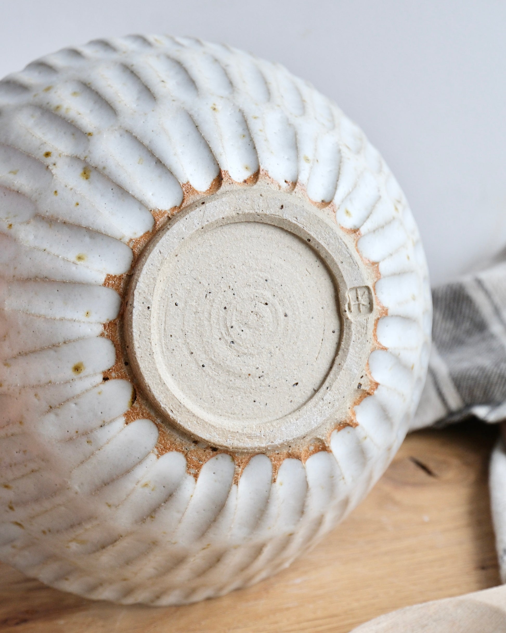 The back of a handmade white stoneware breakfast bowl with a textured carved design on a wooden chopping board