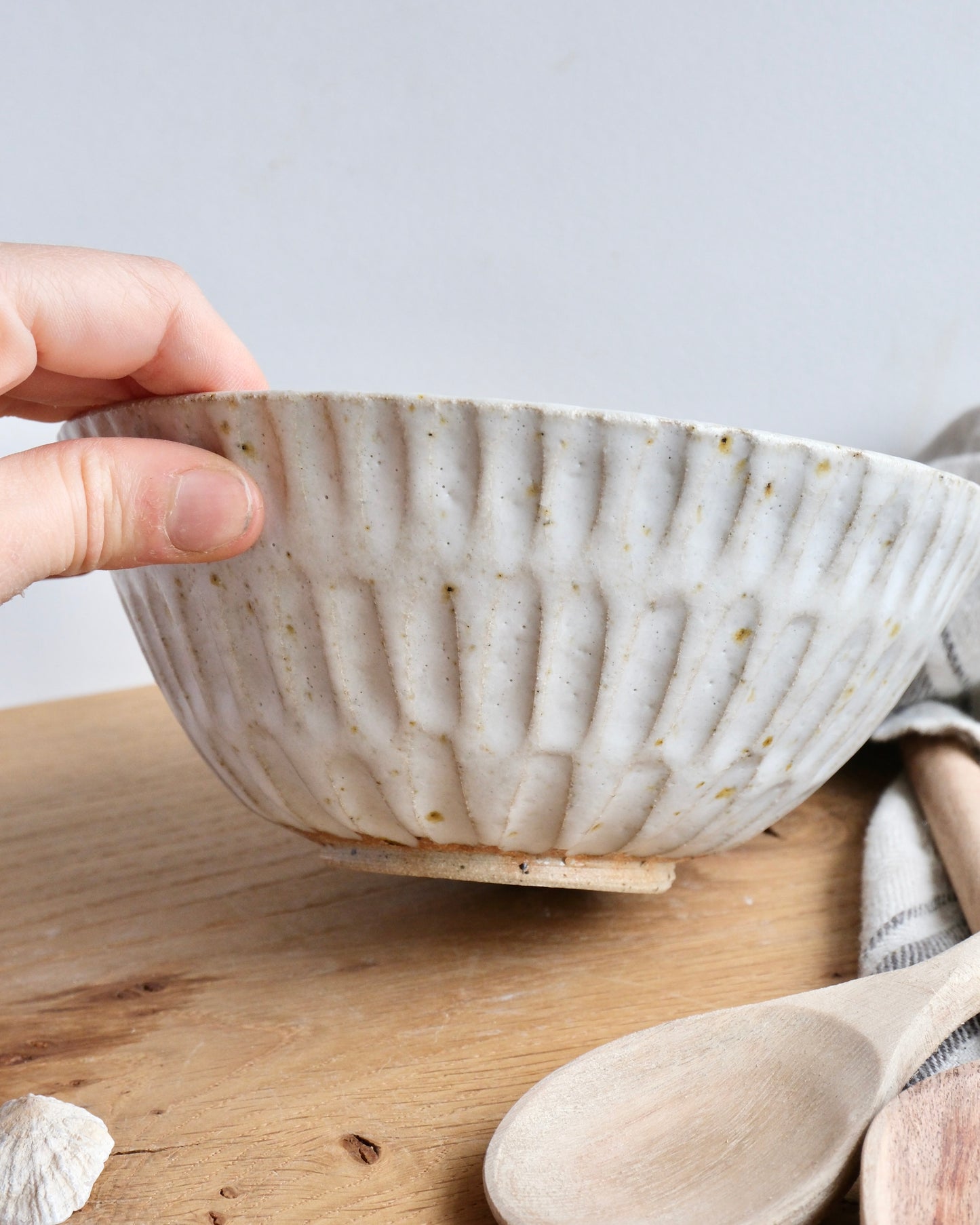 Handmade white stoneware breakfast bowl with a textured carved design on a wooden chopping board