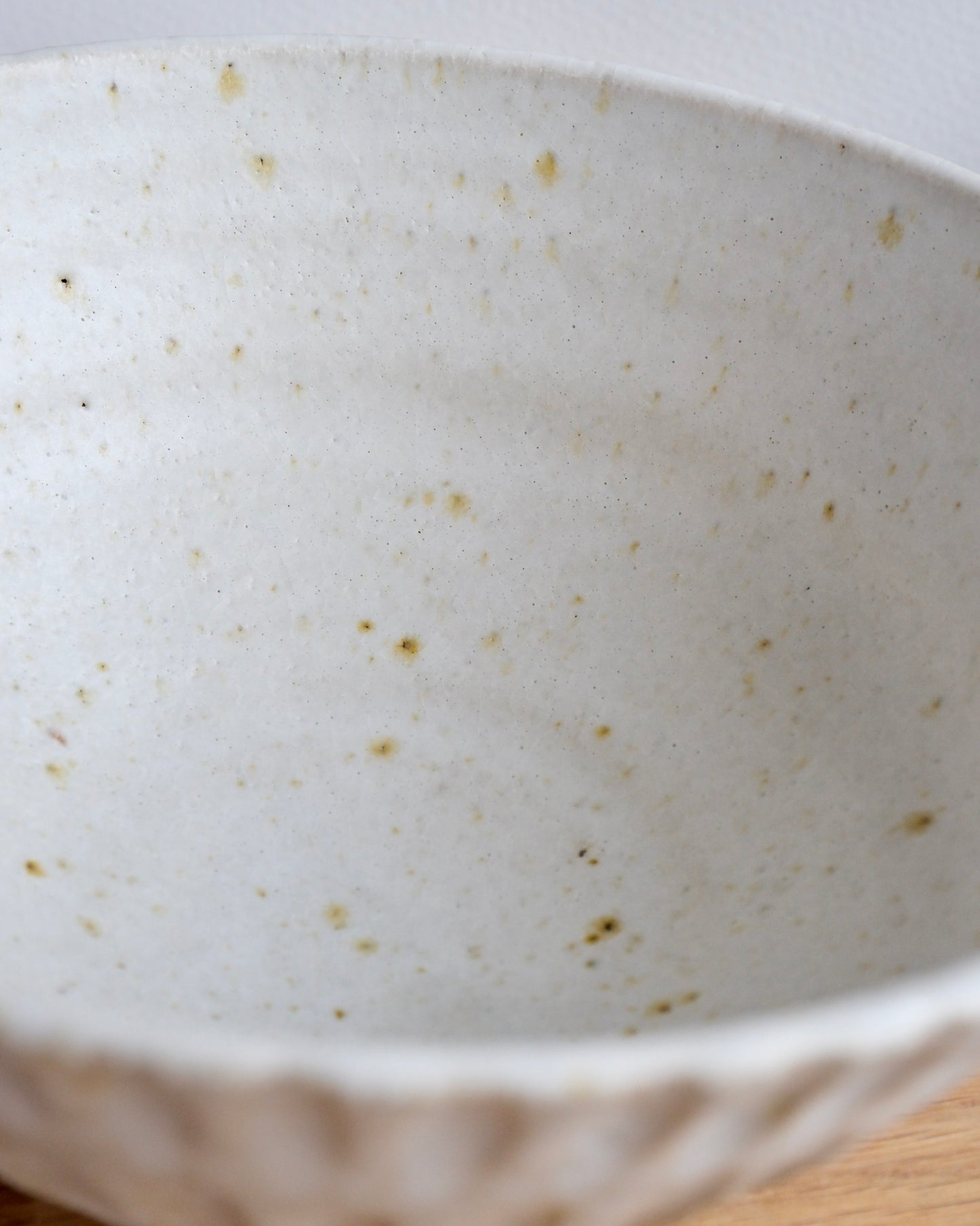 Close up of a handmade white stoneware breakfast bowl with a textured carved design on a wooden chopping board