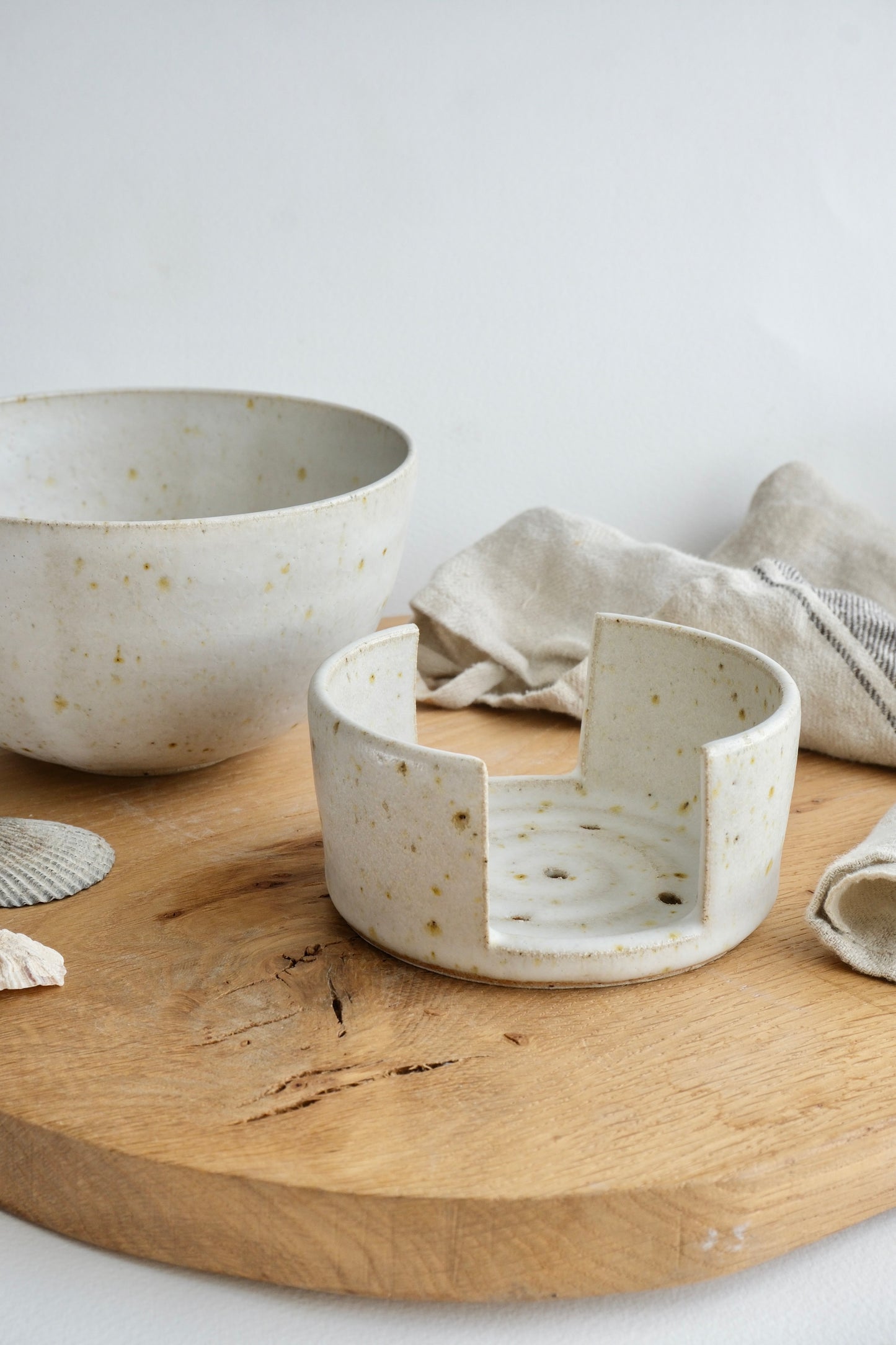 A white speckled ceramic sponge holder and breakfast bowl on a wooden chopping board