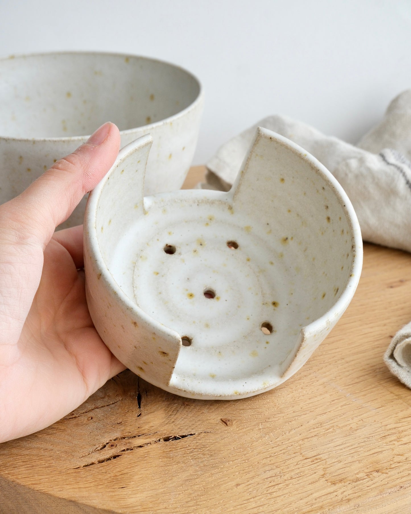 a hand holding a white speckled ceramic sponge holder dish with drainage holes. 