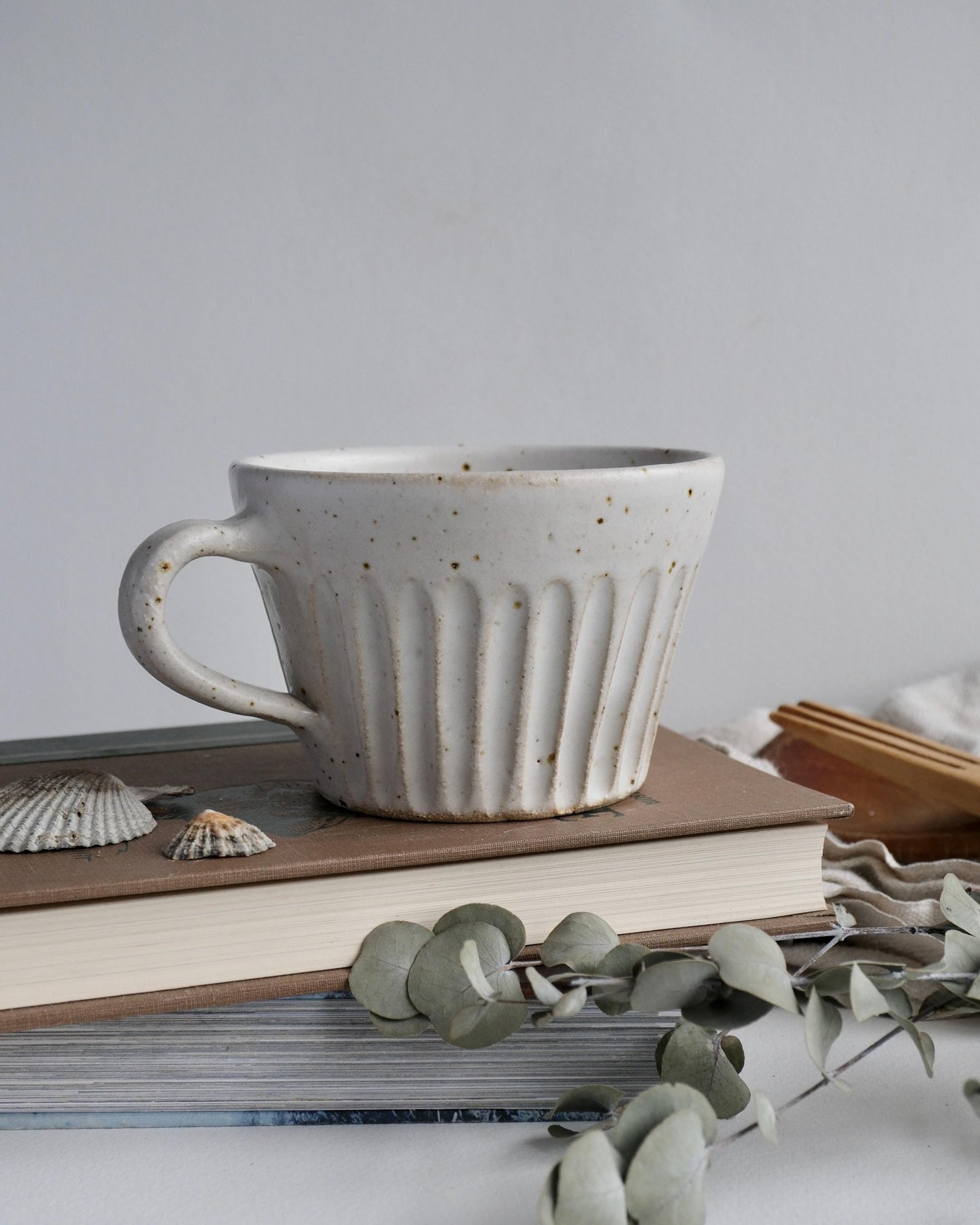 White Ceramic coffee mug on books with eucalyptus leaves on a light surface