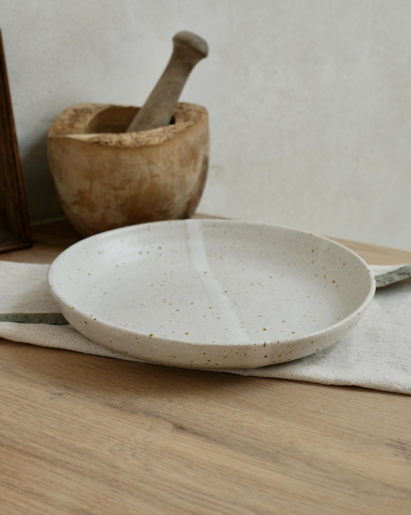 White Ceramic pasta bowl with speckled pattern on a wooden surface with a wooden mortar and pestle in the background.