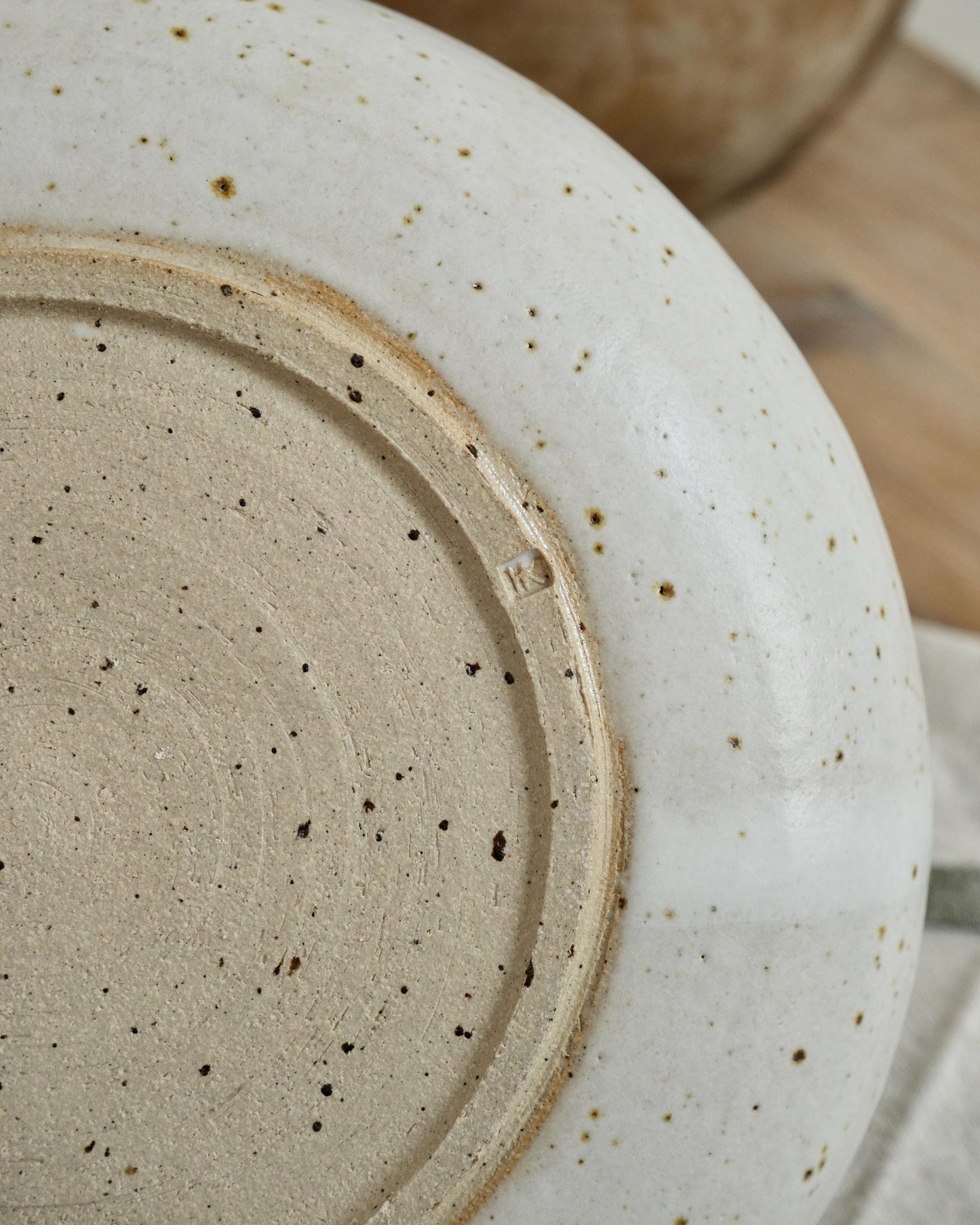 Close-up of a ceramic pasta bowl with speckled texture on a wooden surface