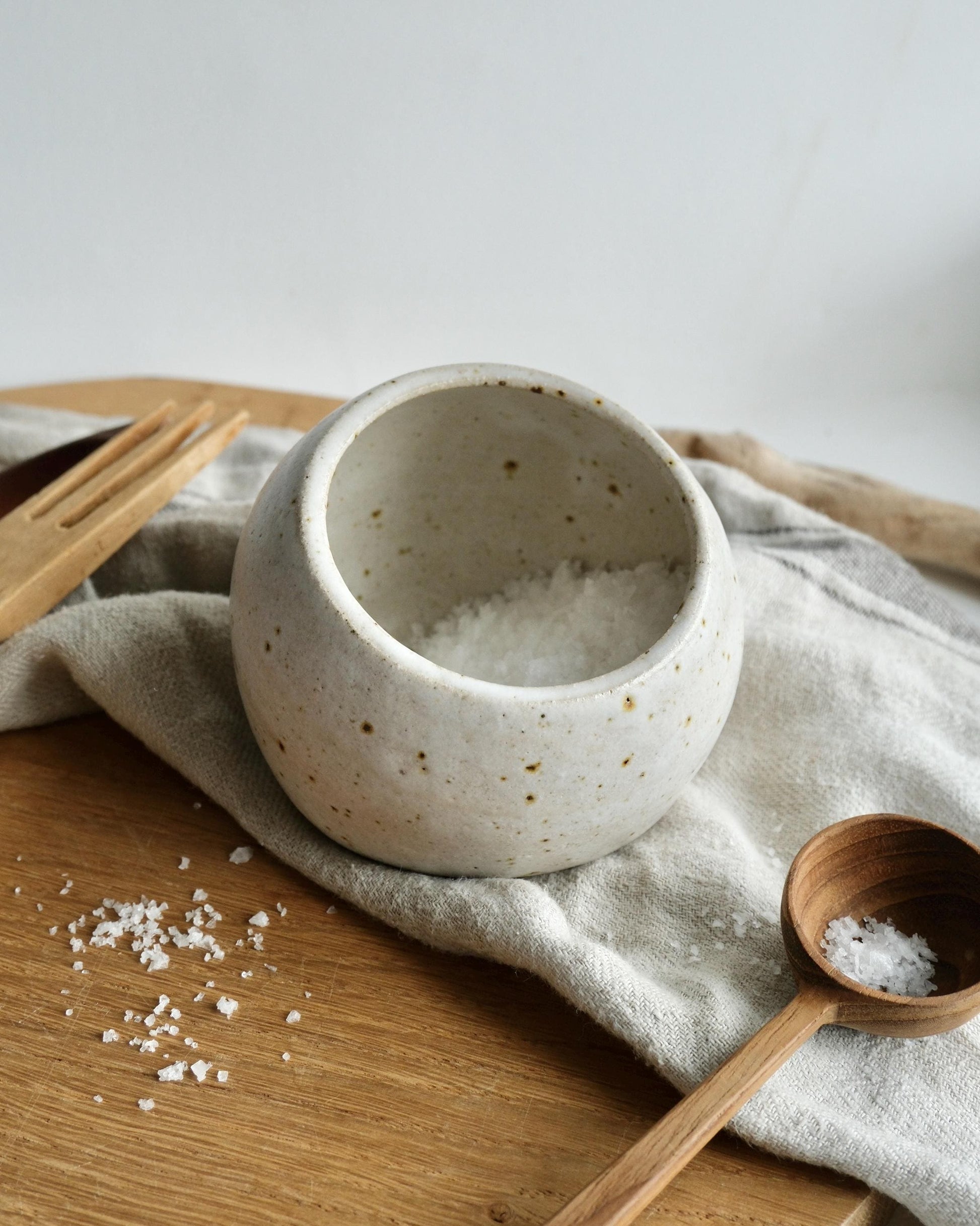 Ceramic white speckled salt cellar with wooden spoon on a wooden surface