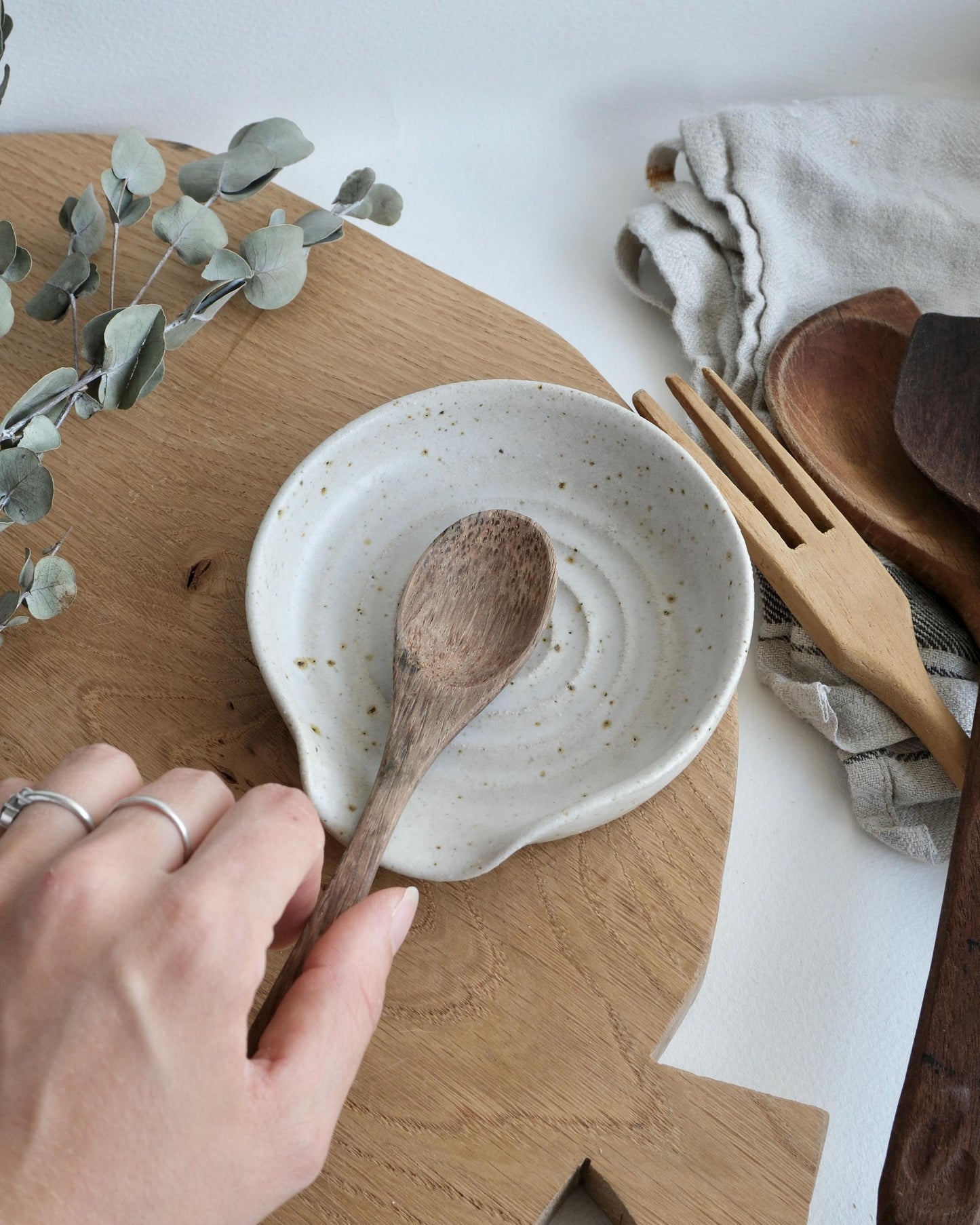 Person holding a wooden spoon over a ceramic dish on a wooden surface with a white background.