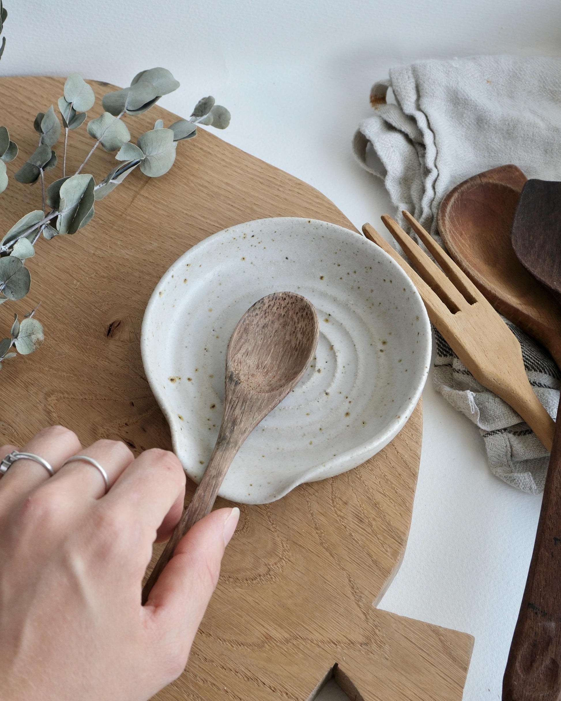 Person holding a wooden spoon over a ceramic dish on a wooden surface with a white background.