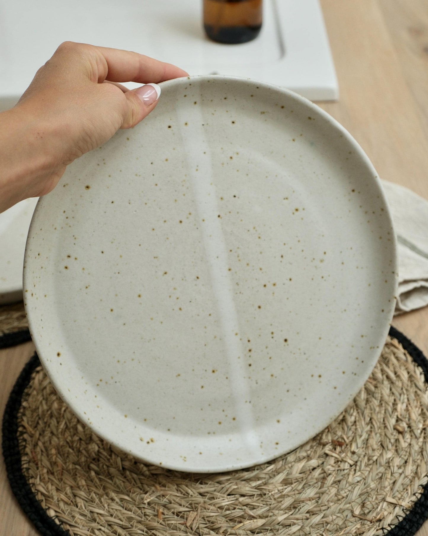 Hand holding a handmade white ceramic plate with a textured surface on a woven mat.