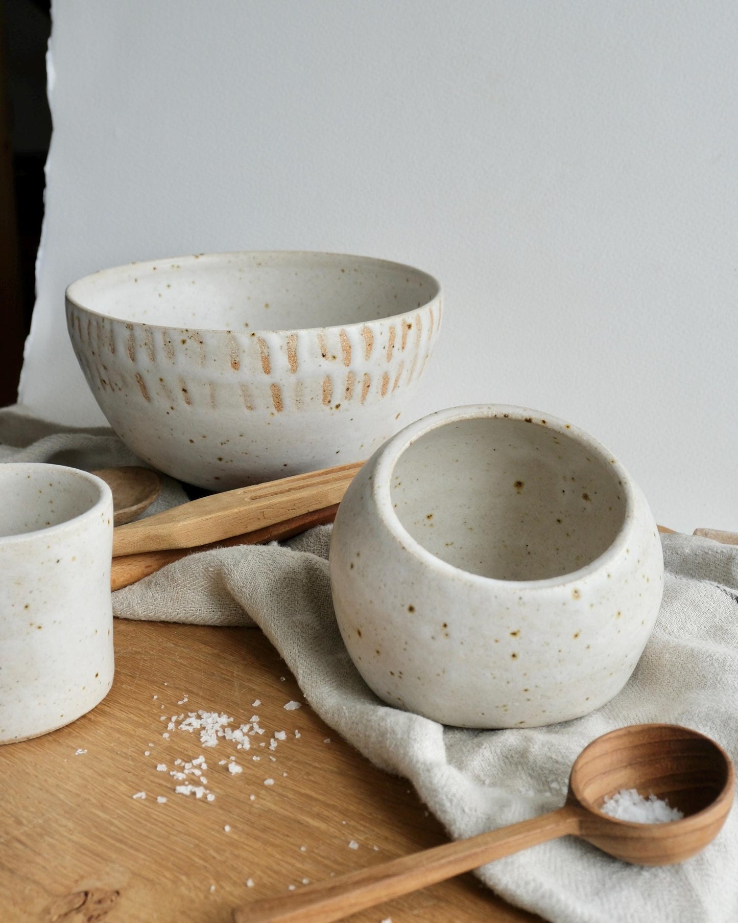 Set of ceramic bowls and slat cellar and a wooden spoon on a wooden surface with a white background
