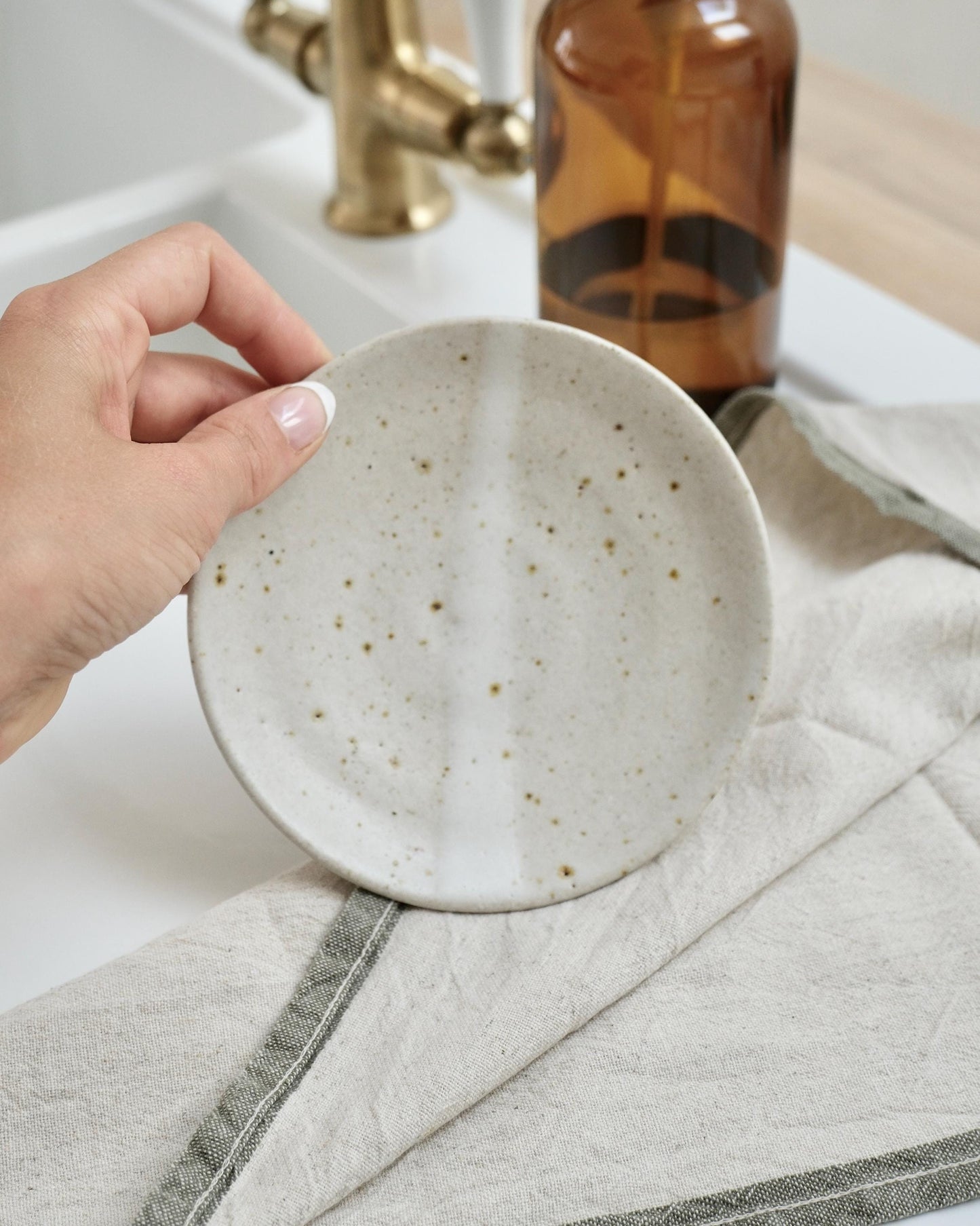 Person holding a white ceramic dish over a sink with a towel and bottle in the background