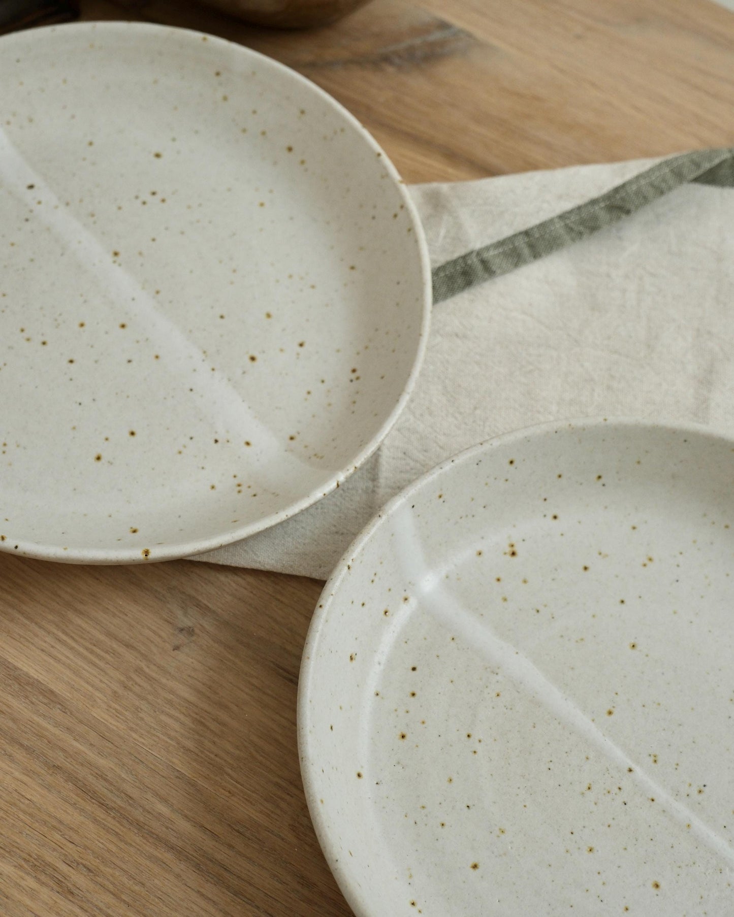 Two white ceramic pasta bowls with speckled texture on a wooden surface.