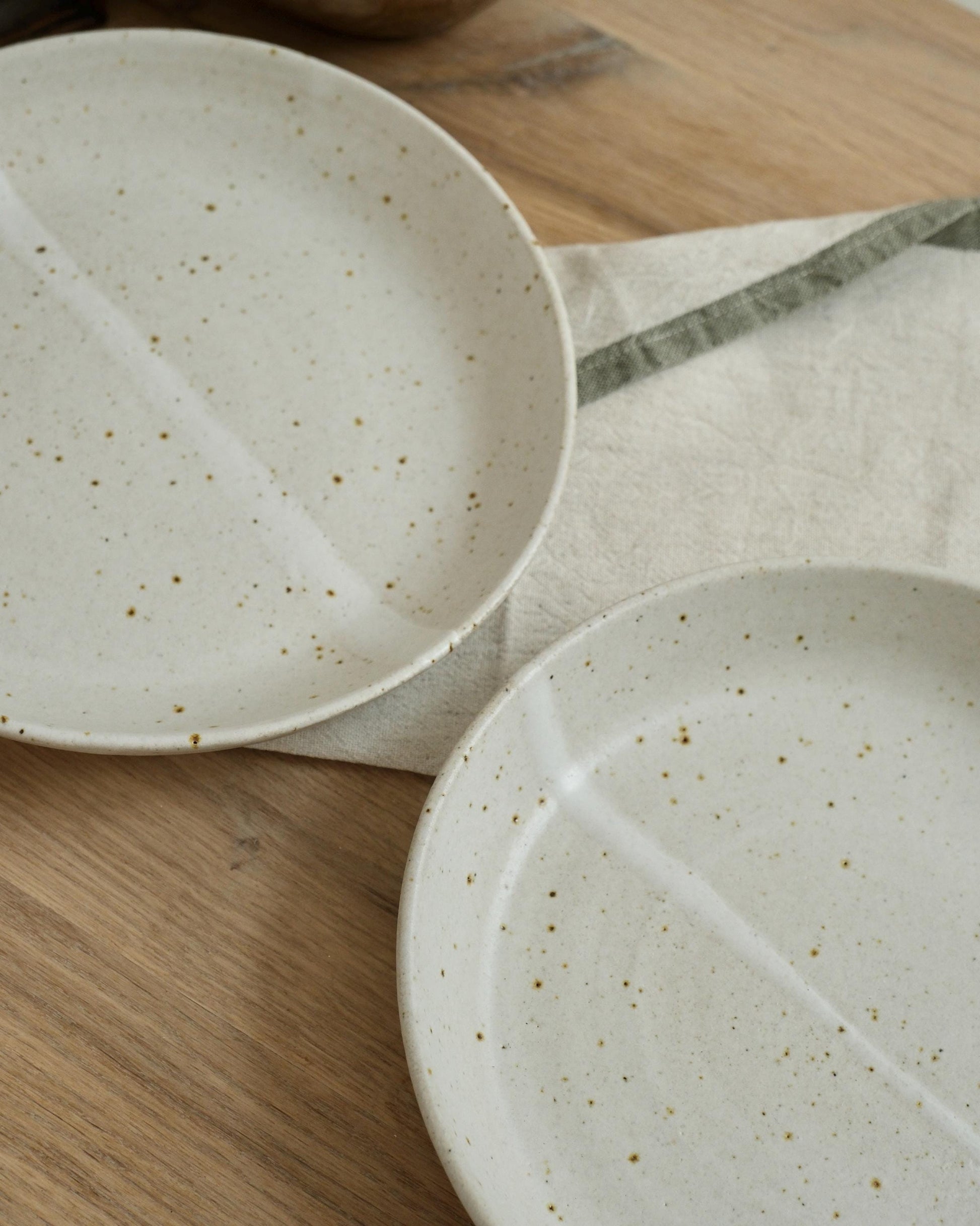 Two white ceramic pasta bowls with speckled texture on a wooden surface.