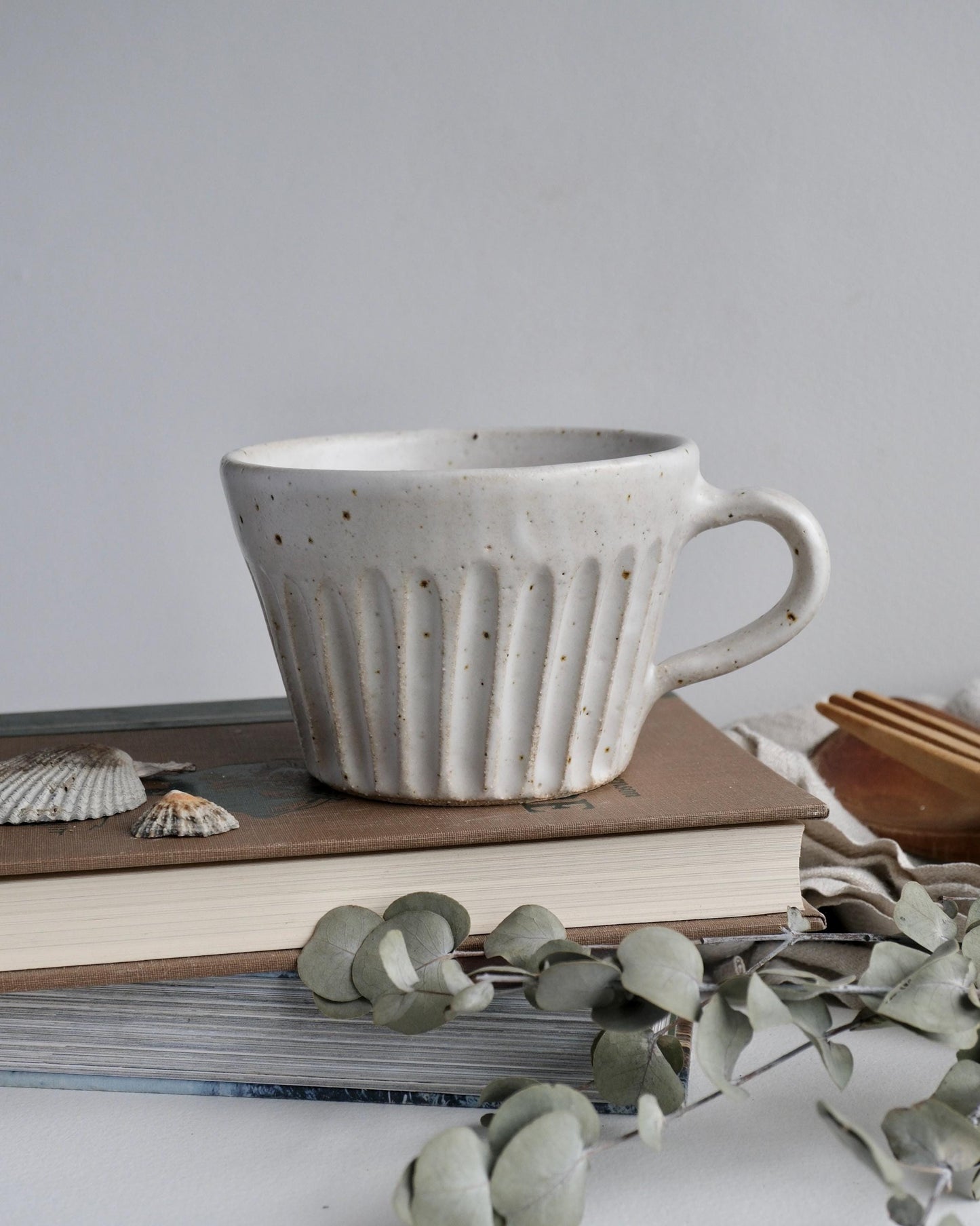White ceramic mug with a line carved pattern on a stack of books with a minimal background