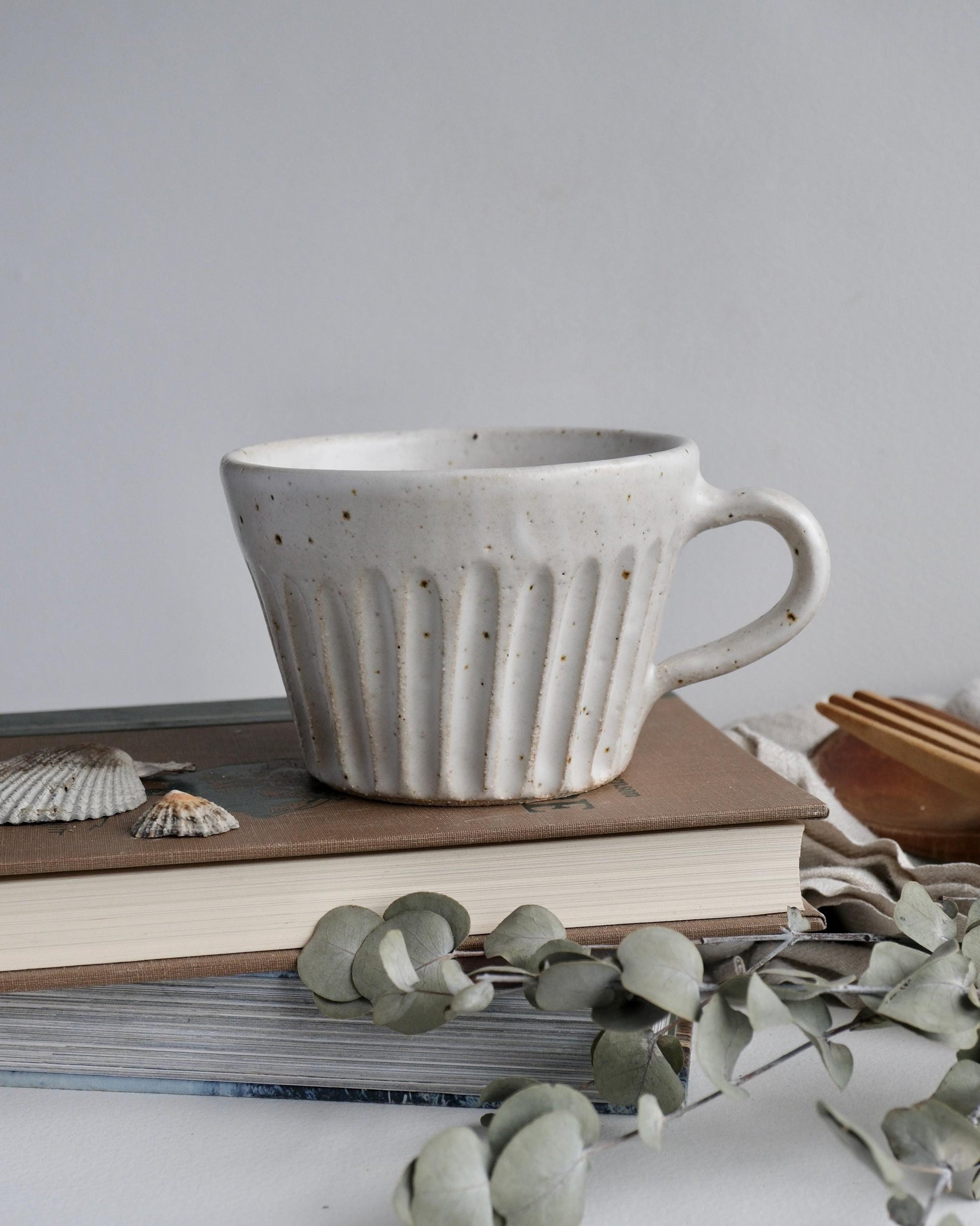 White ceramic mug with a line carved pattern on a stack of books with a minimal background