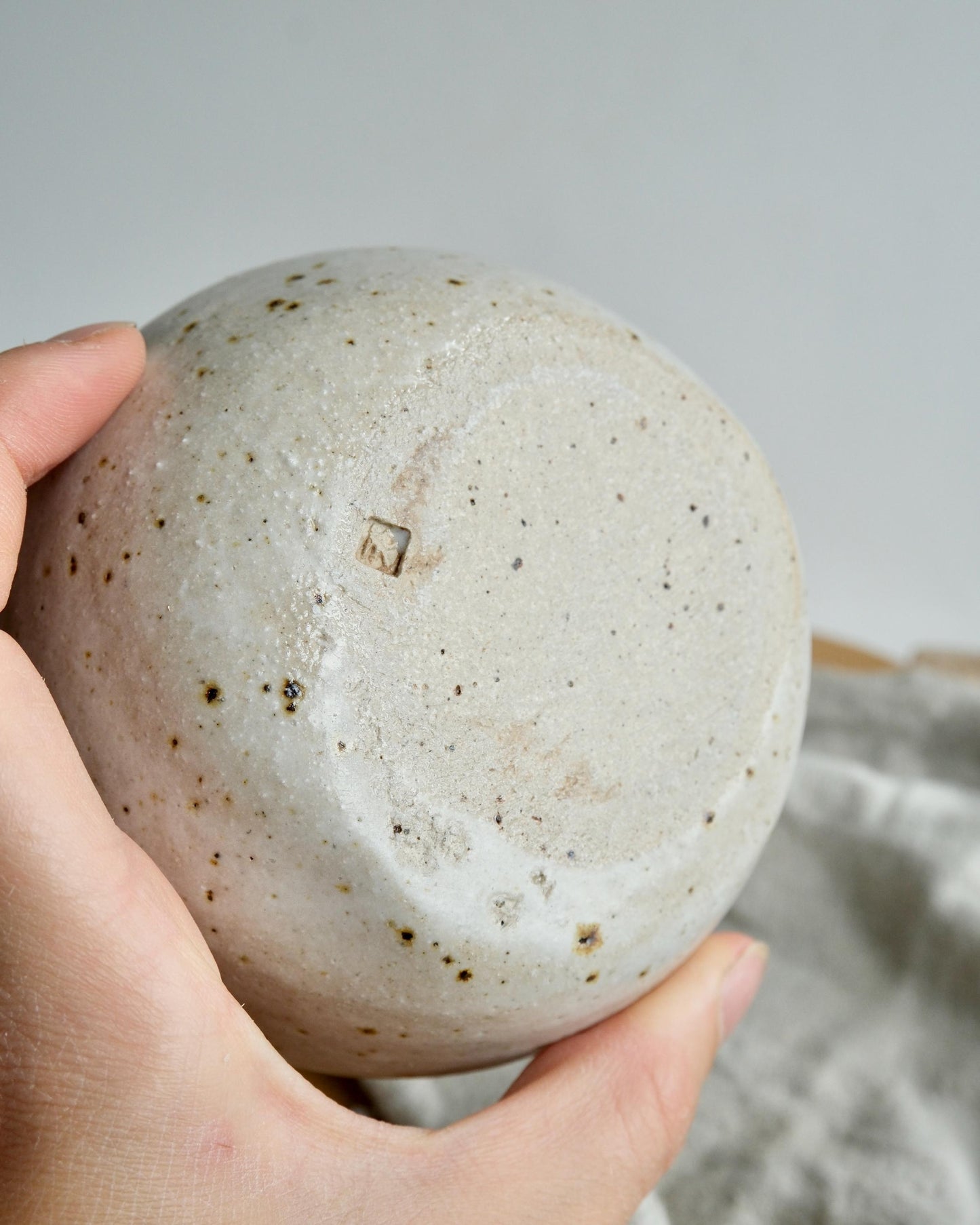 Hand holding a textured ceramic bowl against a neutral background