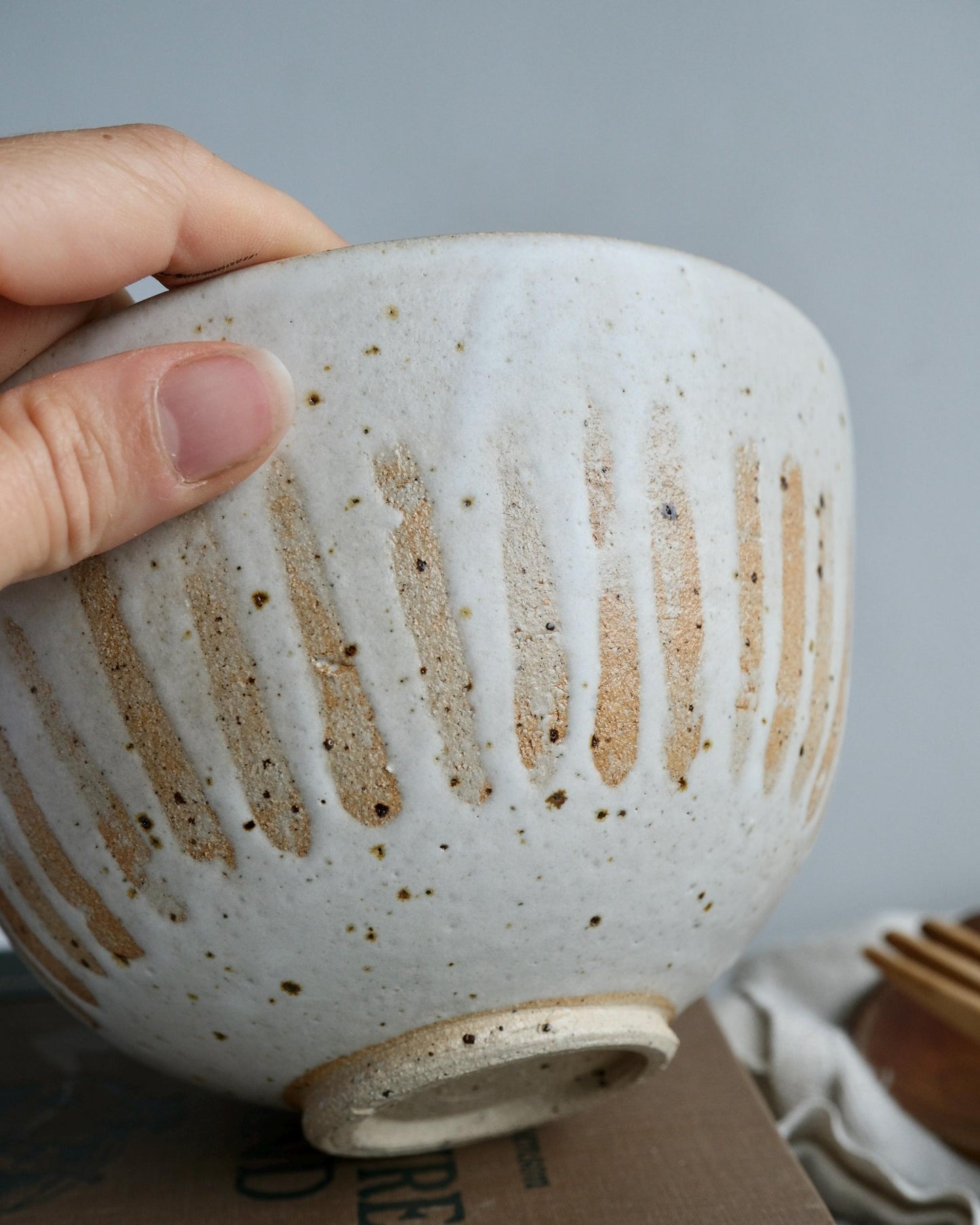 Hand holding a white ceramic bowl with a textured surface against a neutral background