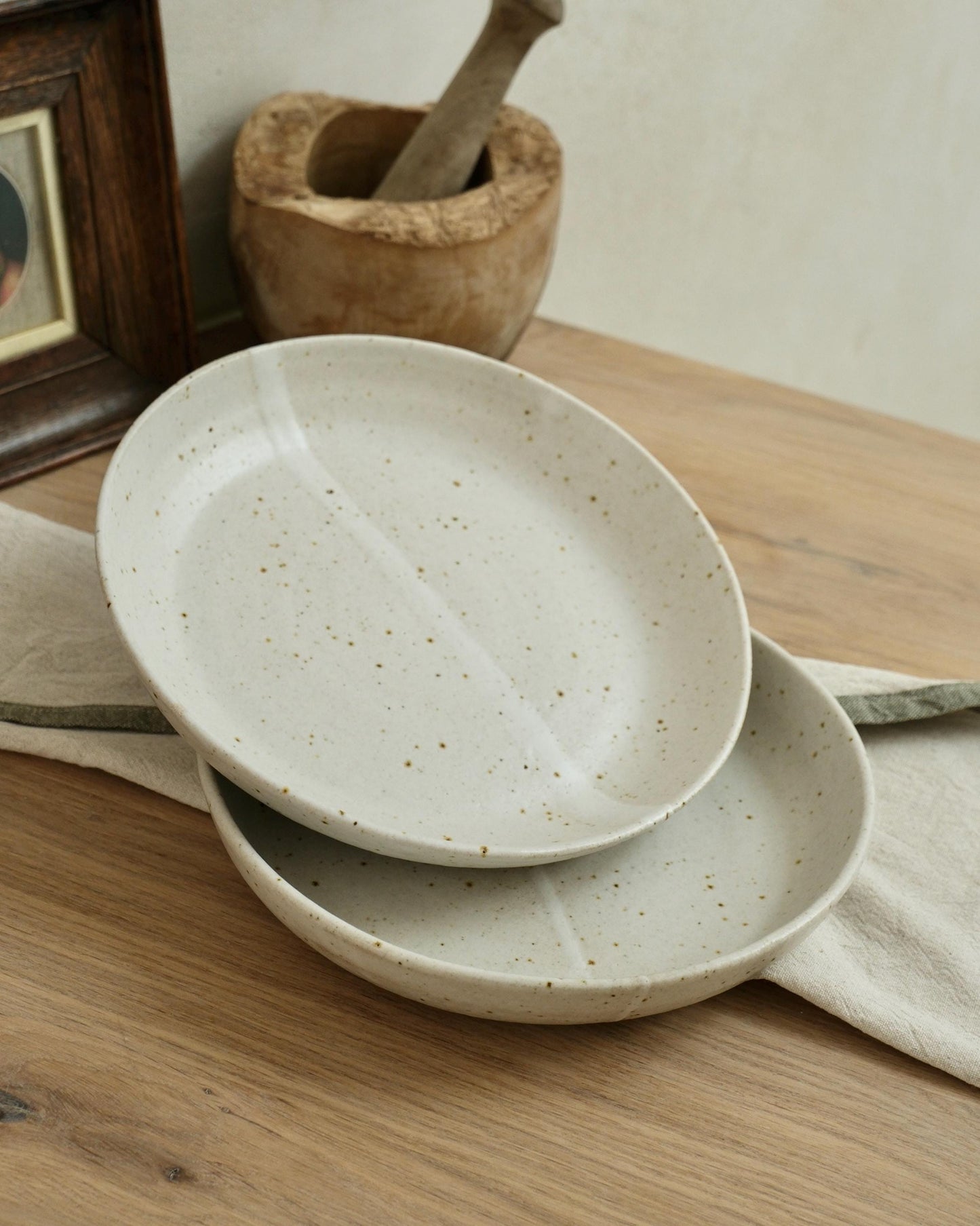 Two white ceramic pasta bowls stacked on a wooden surface with a wooden mortar and pestle in the background.