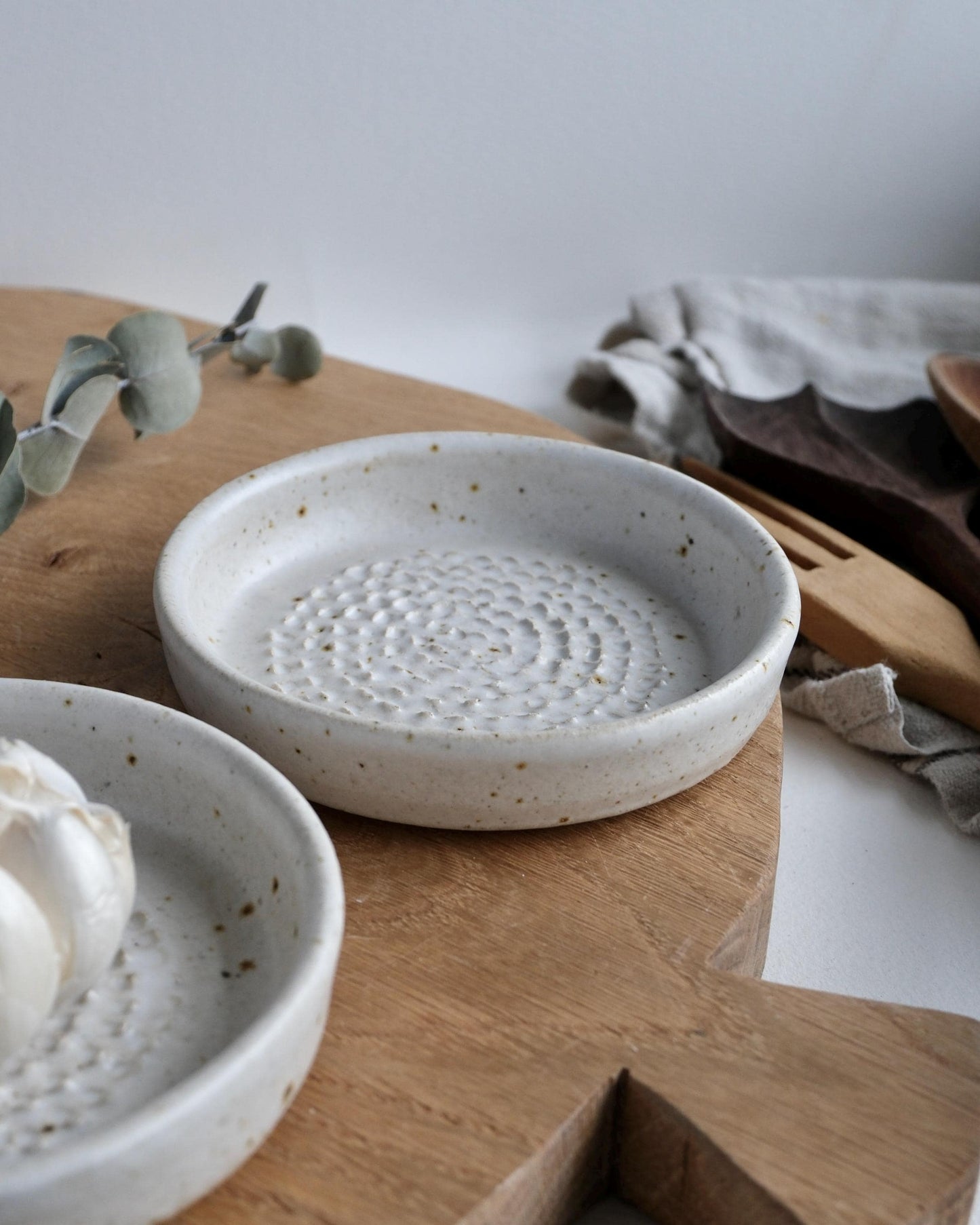Two white ceramic grater dishes on a wooden surface with a neutral background