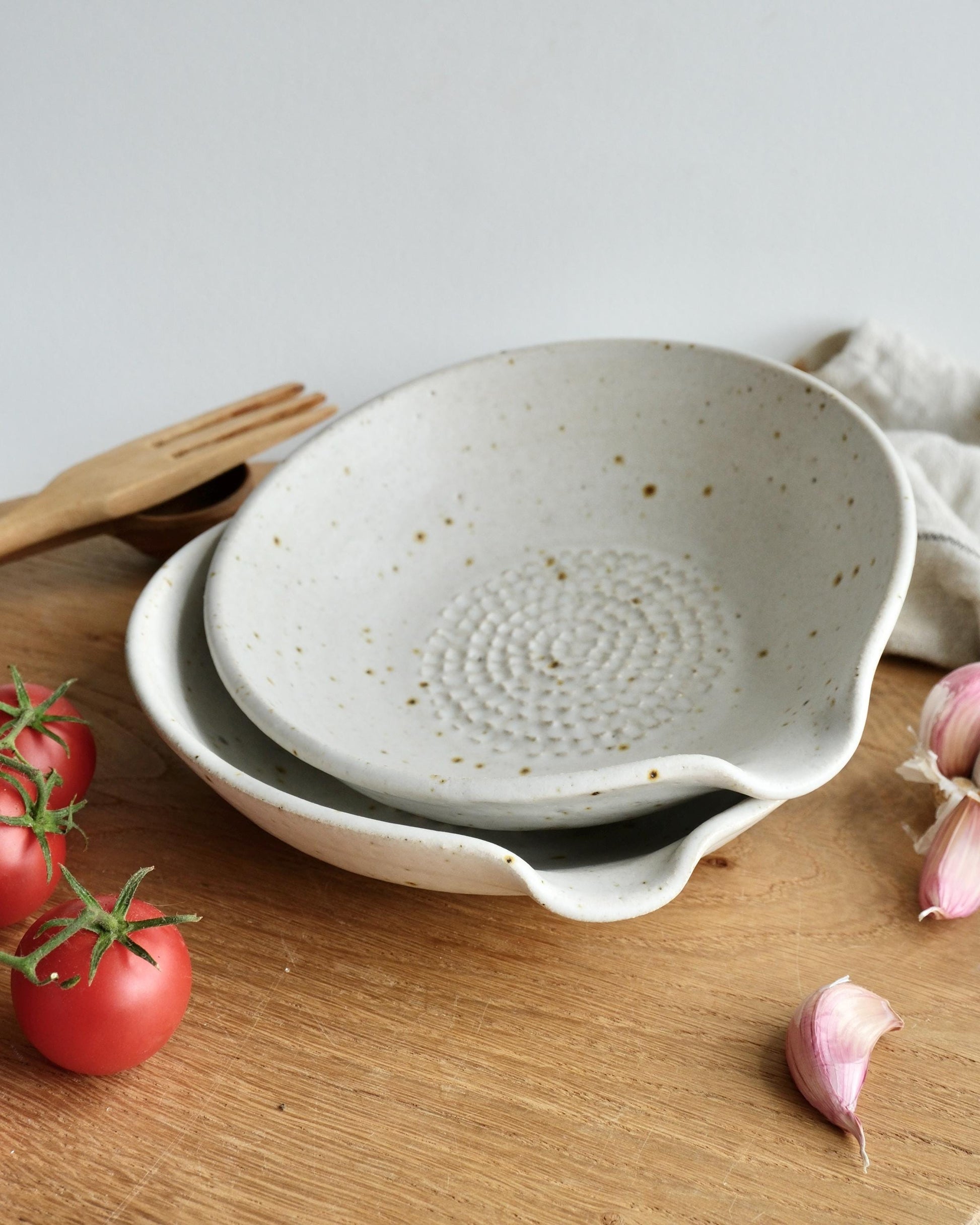 Two ceramic grater dishes on a wooden surface with tomatoes and garlic.