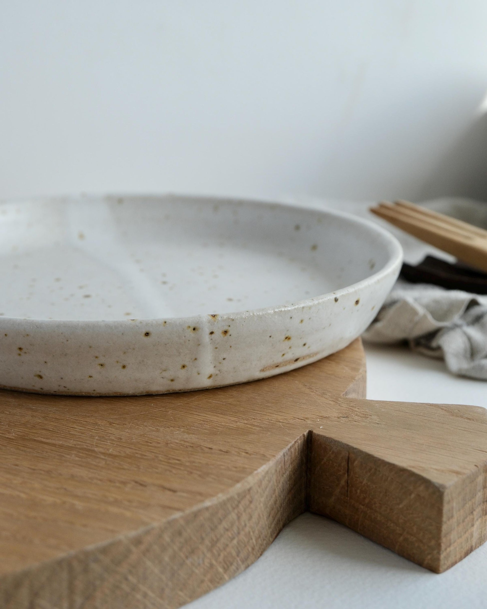 Speckled ceramic small side plate on a wooden cutting board with a neutral background