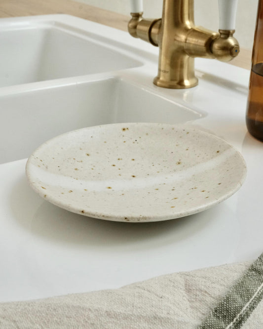 white Speckled ceramic dish on a kitchen counter with a sink and gold faucet in the background.