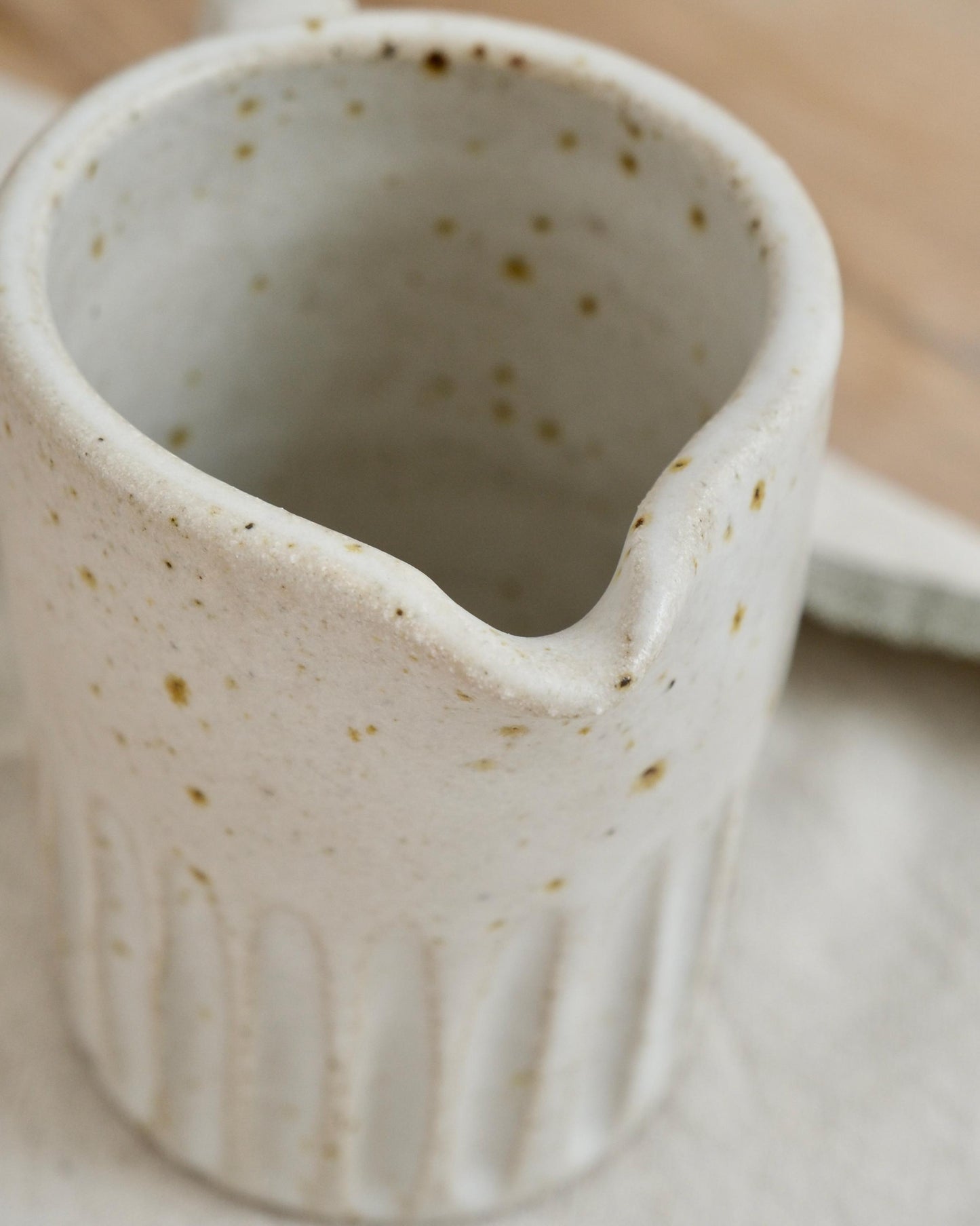 Close-up of a speckled white ceramic pitcher with speckled texture on a neutral background