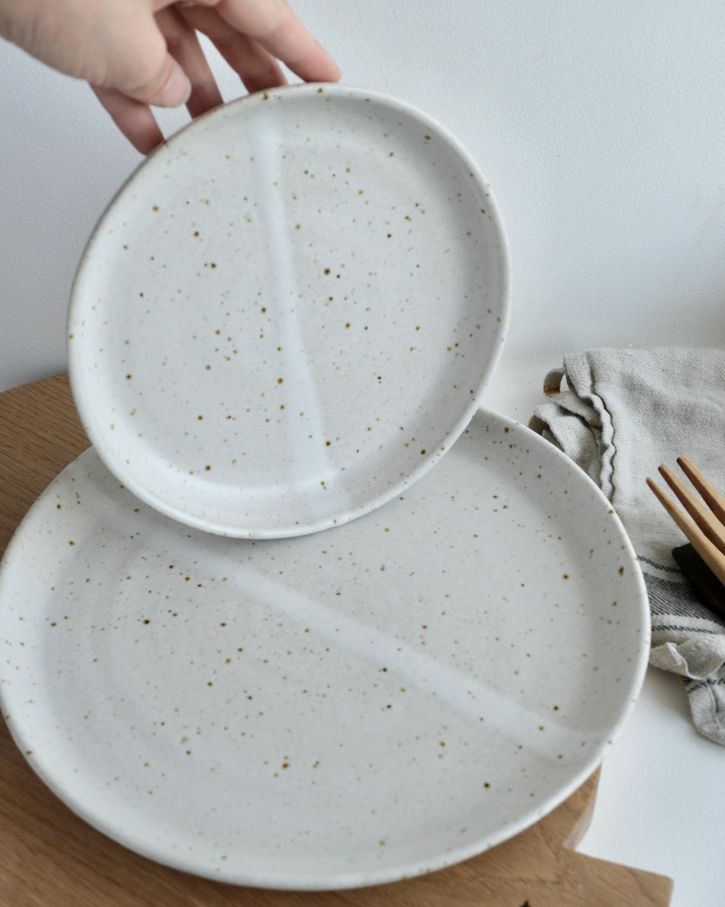 Two speckled ceramic plates on a wooden surface with a hand holding one plate.