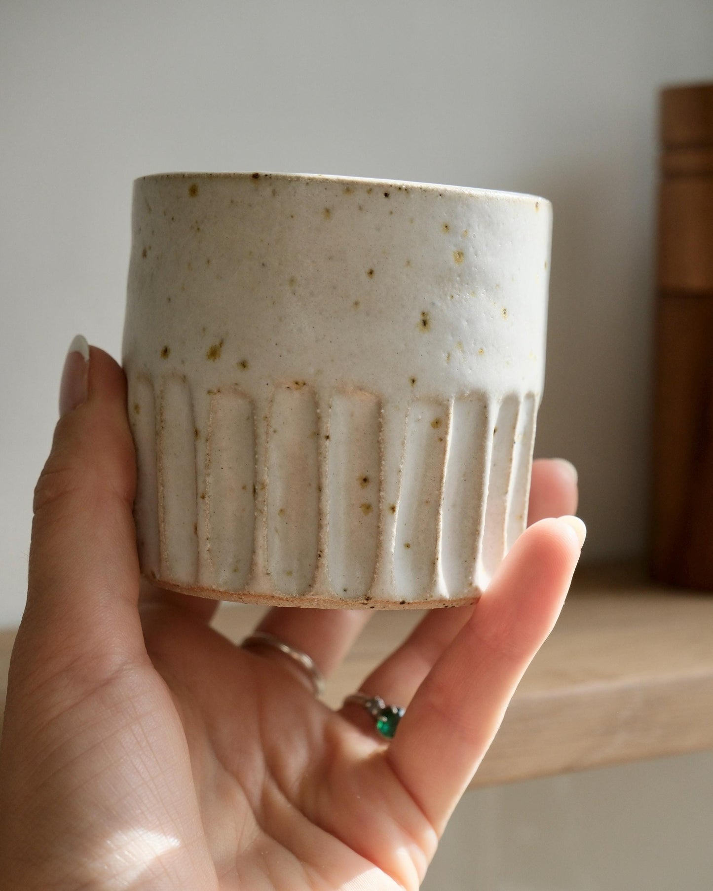Hand holding a ceramic cup with textured line design against a neutral background