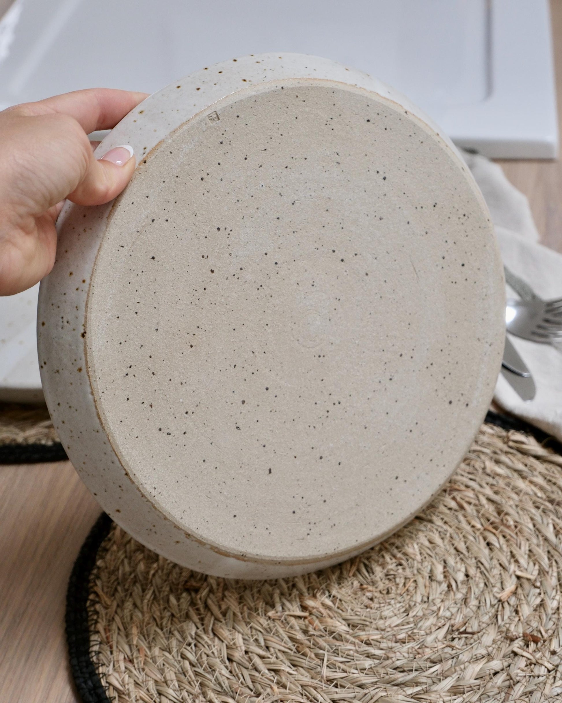 Hand holding a round, speckled ceramic plate on a textured surface