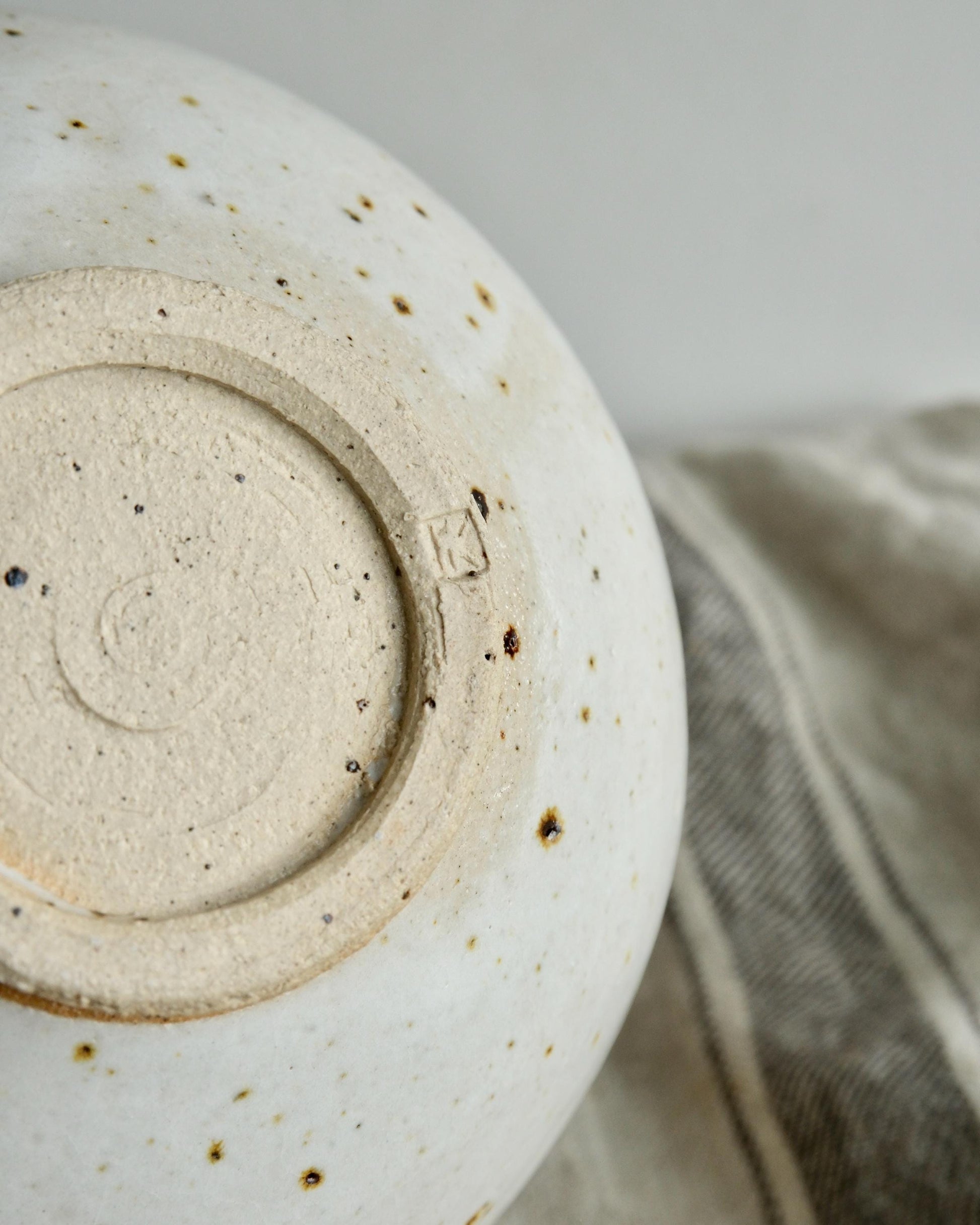Close-up of a ceramic bowl with a textured surface and visible branding on a neutral background.