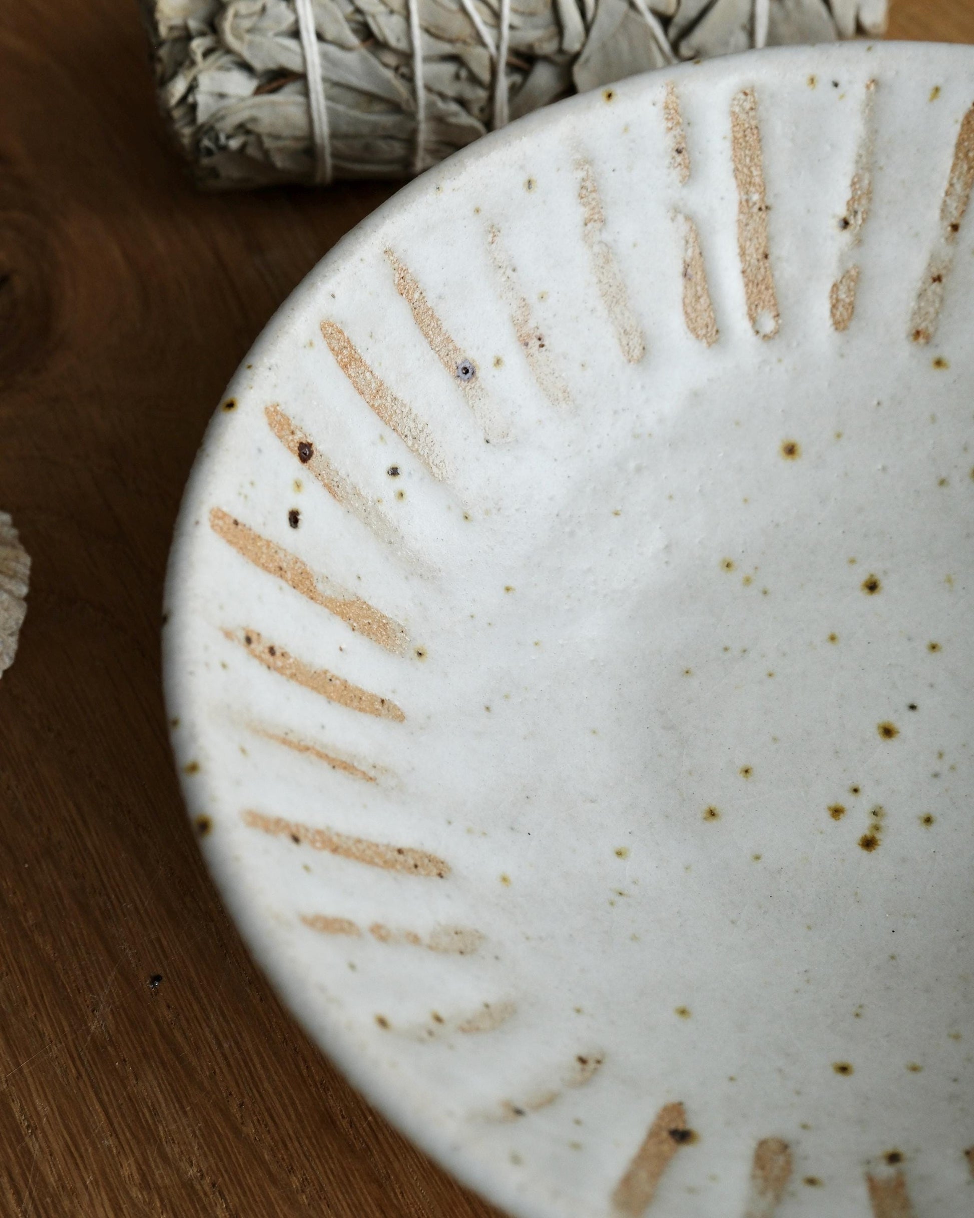 Close-up of a speckled white ceramic trinket dish with textured surface on a wooden surface