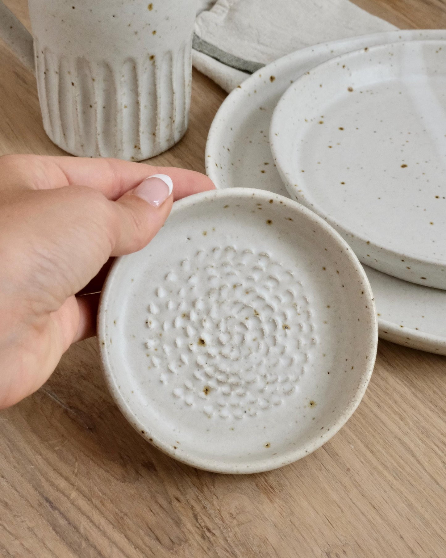Hand holding a white ceramic grater dish with speckled design on a wooden surface