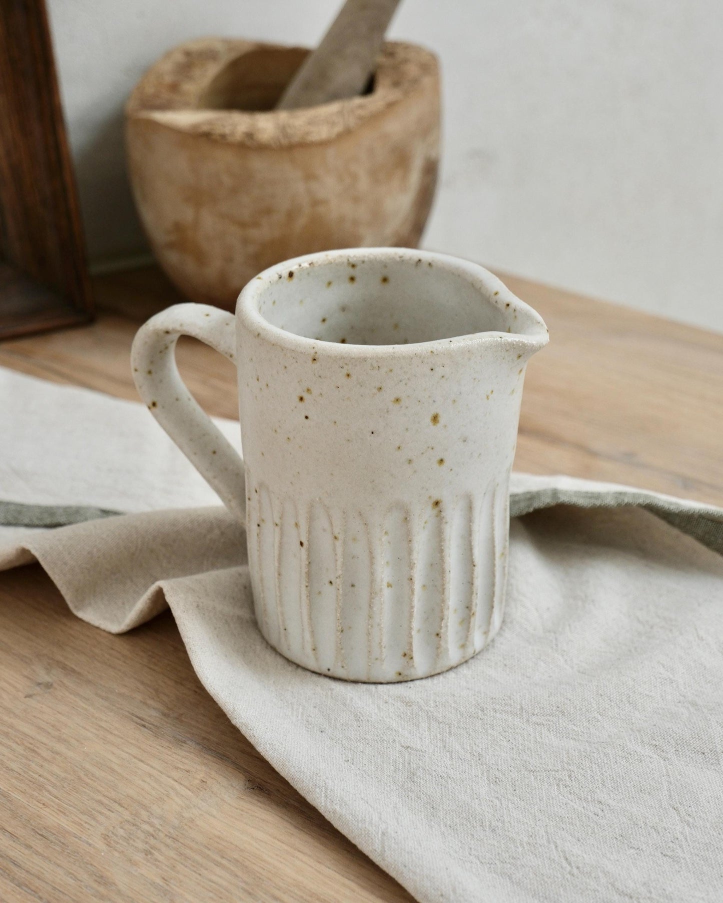 white Speckled ceramic pitcher milk jug on a wooden surface with a cloth
