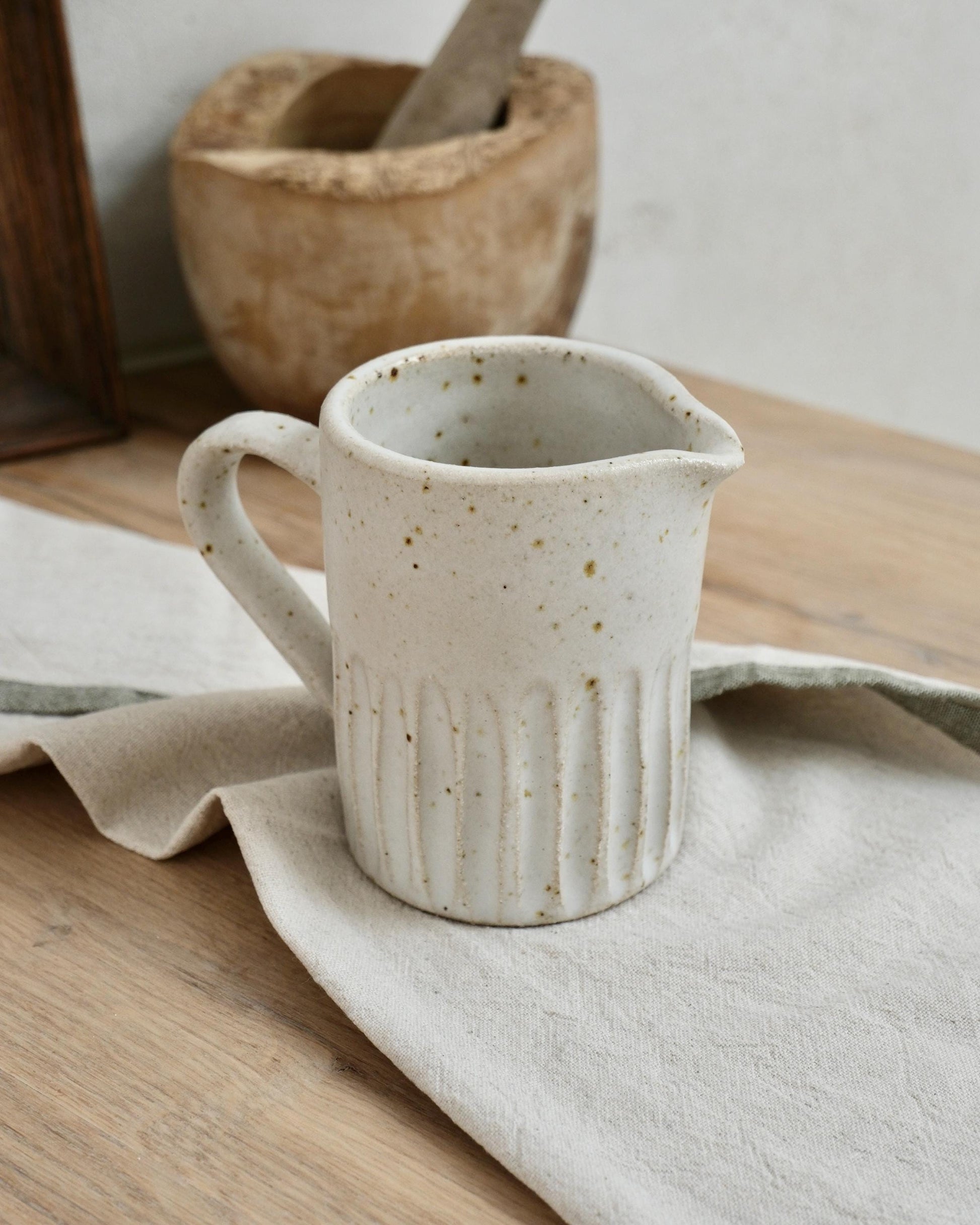 white Speckled ceramic pitcher milk jug on a wooden surface with a cloth