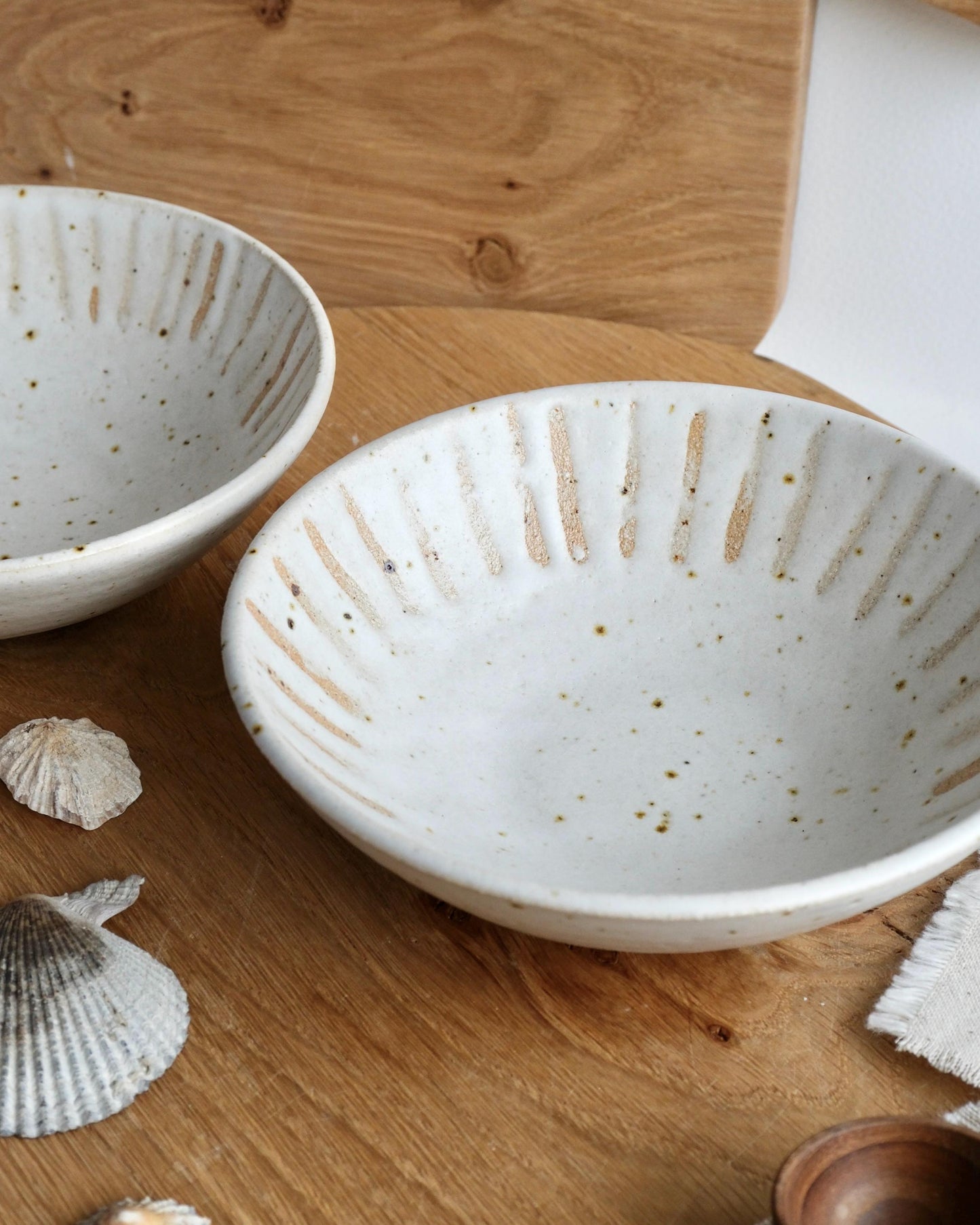 Two white speckled ceramic trinket bowls with orange striped pattern on a wooden surface.