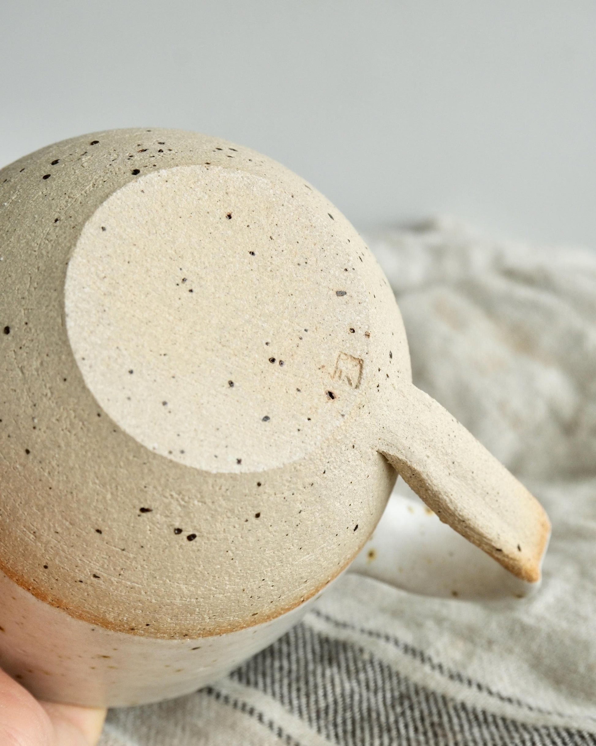 Handmade ceramic mug with a handle, held by a hand on a neutral background