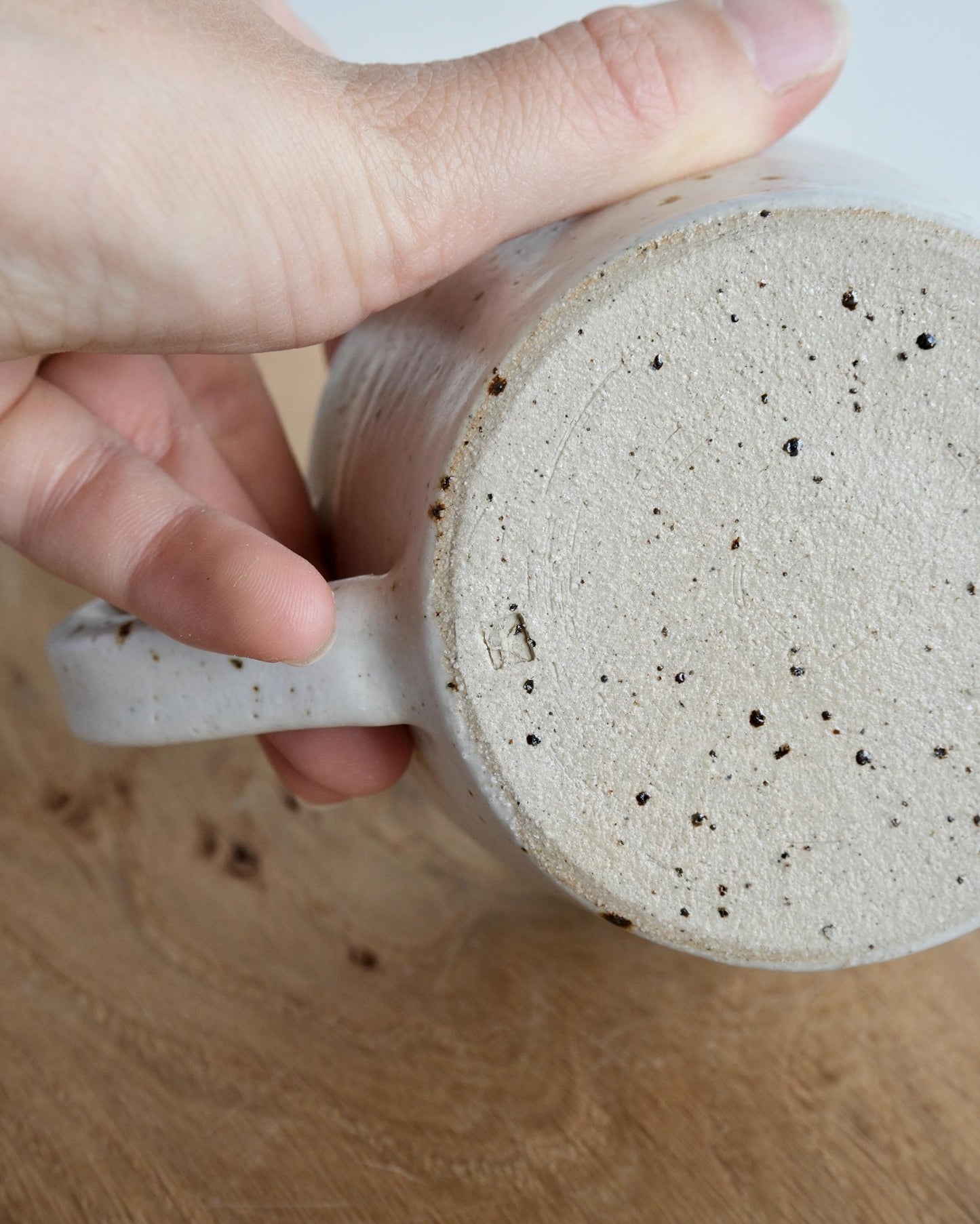 Hand holding a ceramic mug with speckled texture on a wooden surface