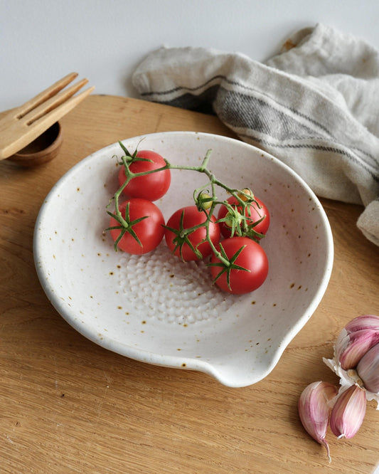 White ceramic garter dish with cherry tomatoes on a wooden surface with garlic and a cloth in the background
