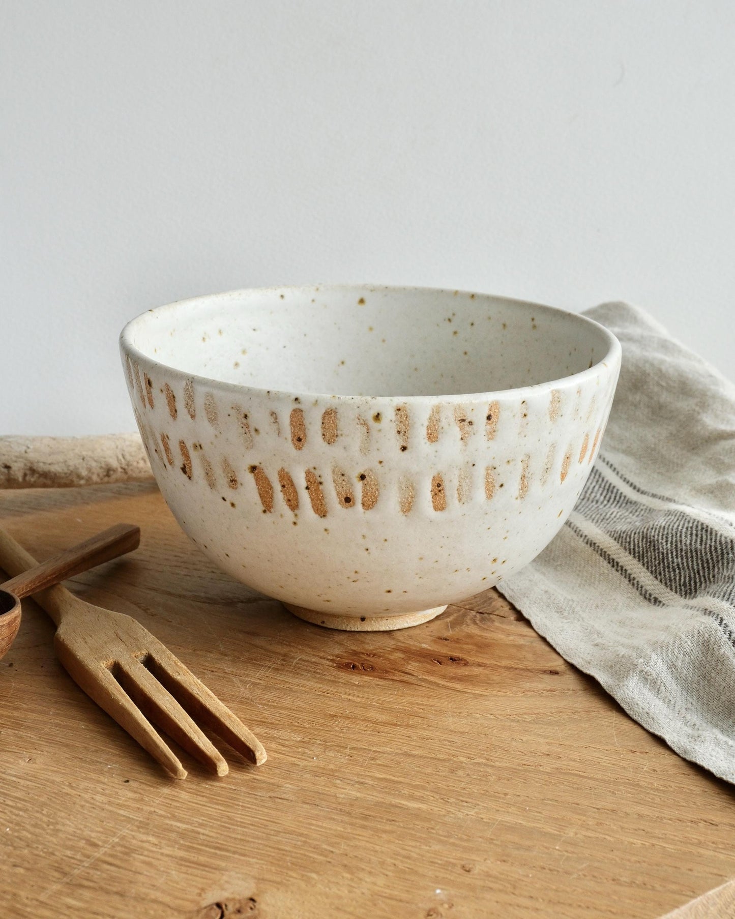 White speckled ceramic breakfast bowl with orange dot speckles on the rim on a wooden surface with a light gray background