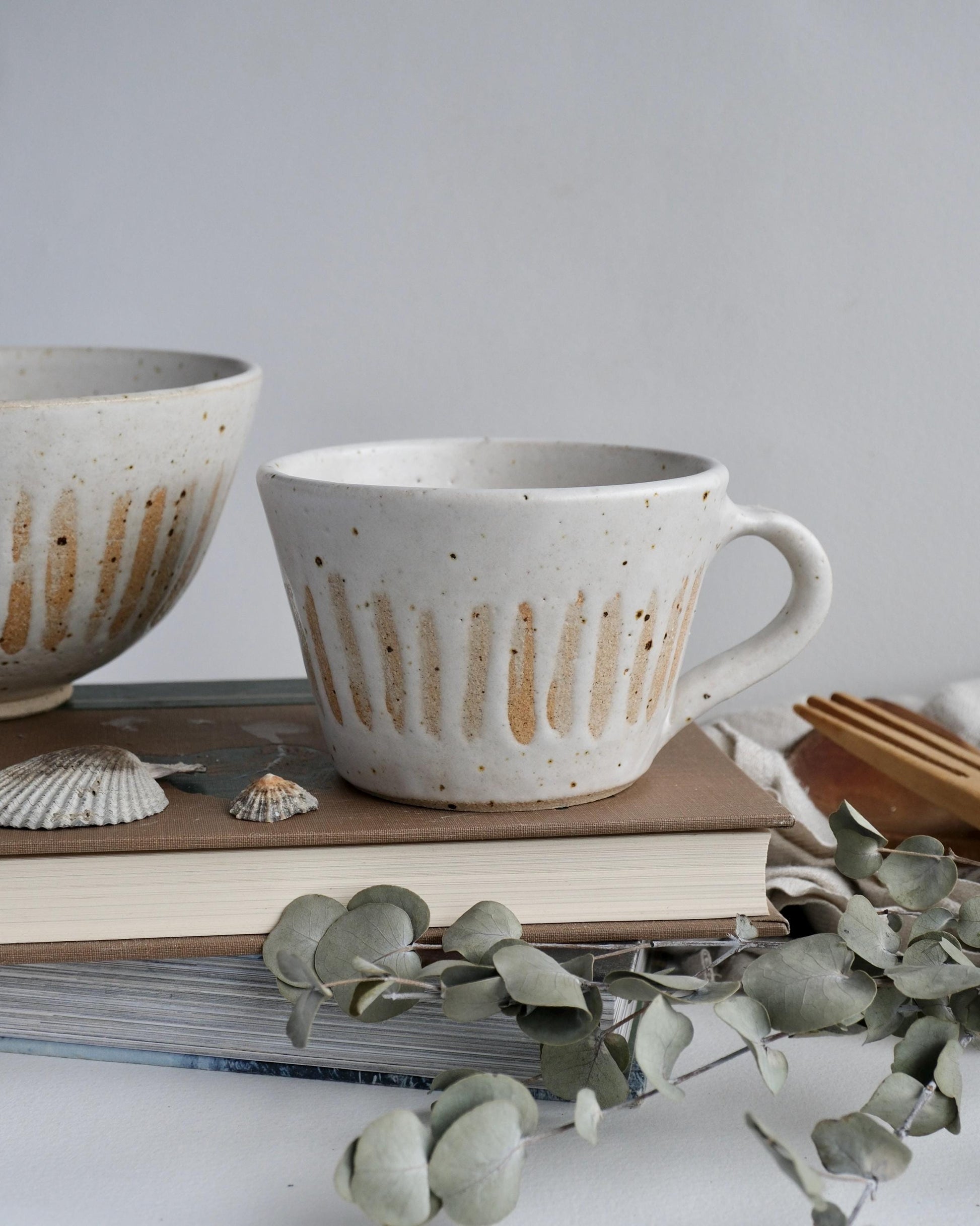 white Speckled orange striped ceramic mug and bowl on a surface with books and greenery